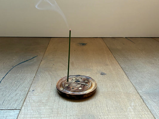 A single EcoIncense stick burning gently in a wooden holder on a natural oak floor, with soft smoke rising — symbolising calm and mindfulness.